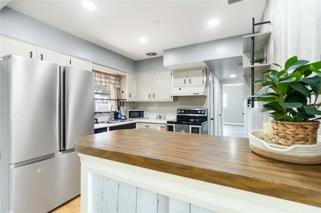 kitchen with white cabinets, a sink, appliances with stainless steel finishes, under cabinet range hood, and butcher block counters