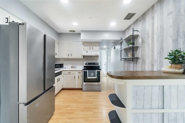 kitchen featuring light wood finished floors, under cabinet range hood, open shelves, visible vents, and appliances with stainless steel finishes