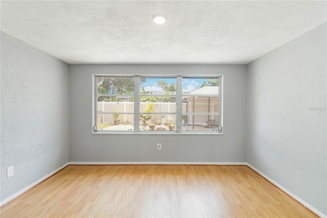 empty room with a textured ceiling, wood finished floors, and baseboards