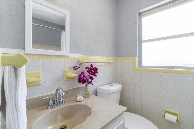 full bath with tile walls, toilet, vanity, and a wainscoted wall