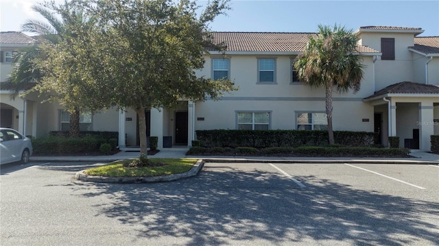 view of front of property with a tiled roof, uncovered parking, and stucco siding