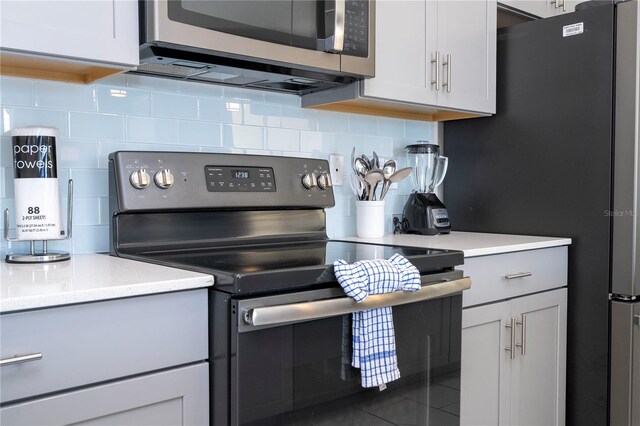 kitchen featuring decorative backsplash, appliances with stainless steel finishes, white cabinets, and dark tile patterned flooring