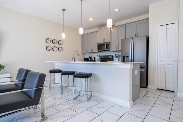 kitchen featuring a kitchen bar, hanging light fixtures, stainless steel appliances, gray cabinets, and a center island with sink