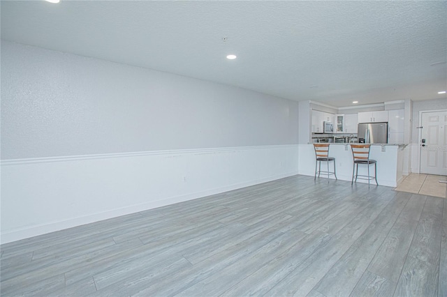 unfurnished living room with a textured ceiling and light hardwood / wood-style floors