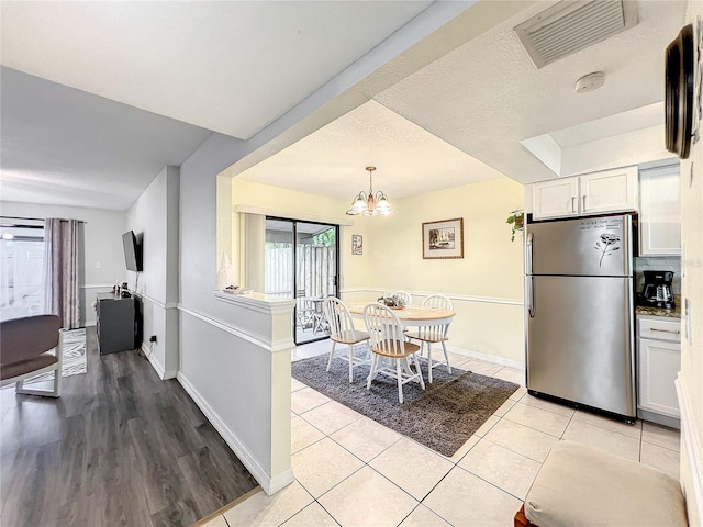 kitchen with light wood-type flooring, hanging light fixtures, white cabinetry, stainless steel fridge, and a notable chandelier