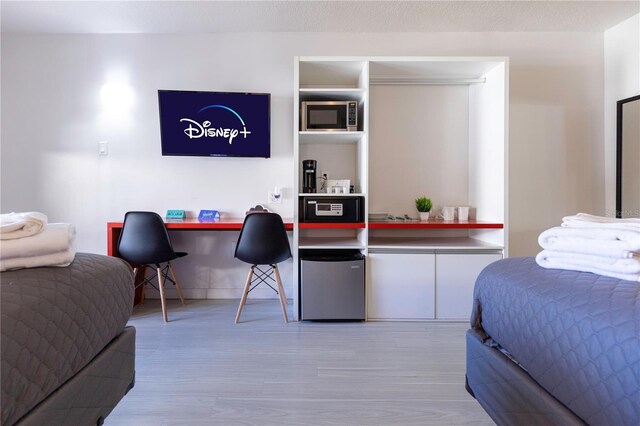 bedroom featuring built in desk, light hardwood / wood-style floors, and stainless steel refrigerator