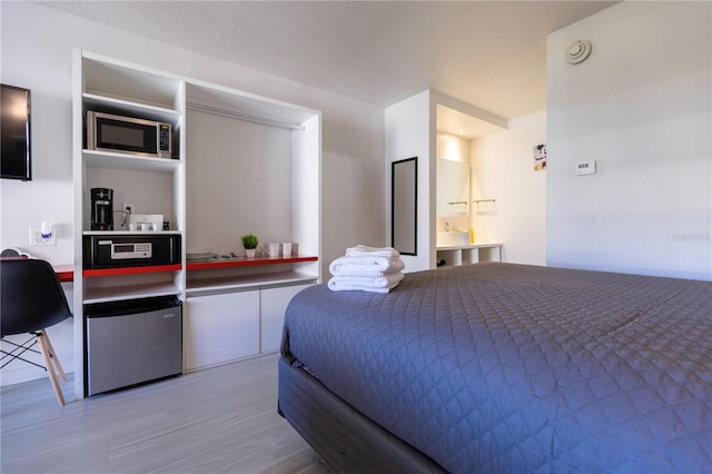 bedroom with stainless steel fridge, hardwood / wood-style flooring, a textured ceiling, and ensuite bath