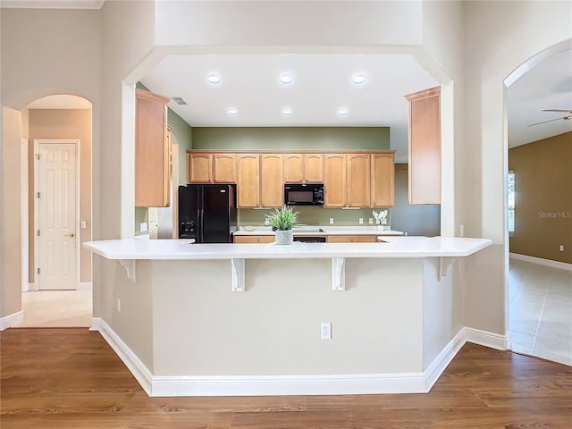 kitchen featuring a kitchen breakfast bar, kitchen peninsula, ceiling fan, and black appliances