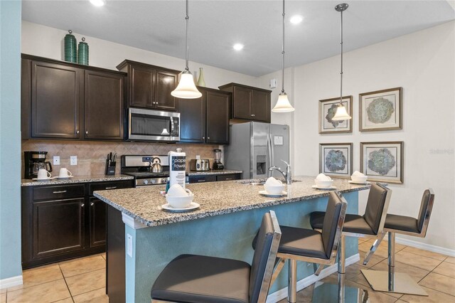 kitchen featuring a breakfast bar area, appliances with stainless steel finishes, pendant lighting, and an island with sink