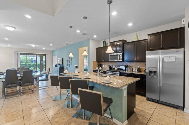 kitchen with a center island with sink, appliances with stainless steel finishes, a kitchen bar, pendant lighting, and light stone counters