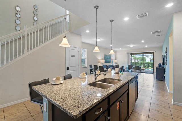 kitchen featuring dishwasher, sink, light stone counters, light tile patterned floors, and a kitchen island with sink