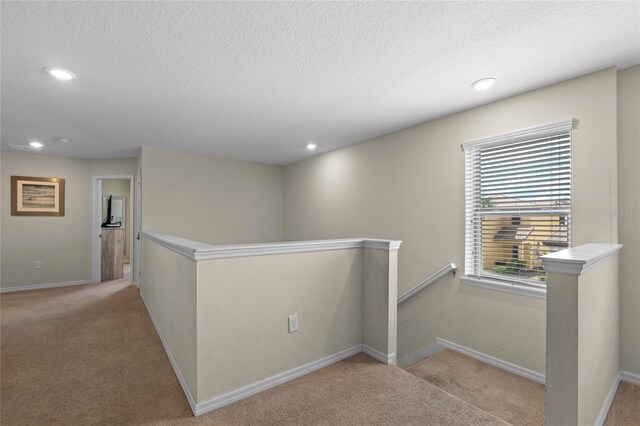 corridor featuring light carpet and a textured ceiling