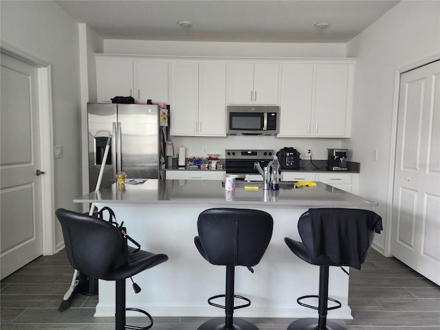 kitchen with stainless steel appliances, dark hardwood / wood-style floors, white cabinets, a breakfast bar area, and a kitchen island with sink