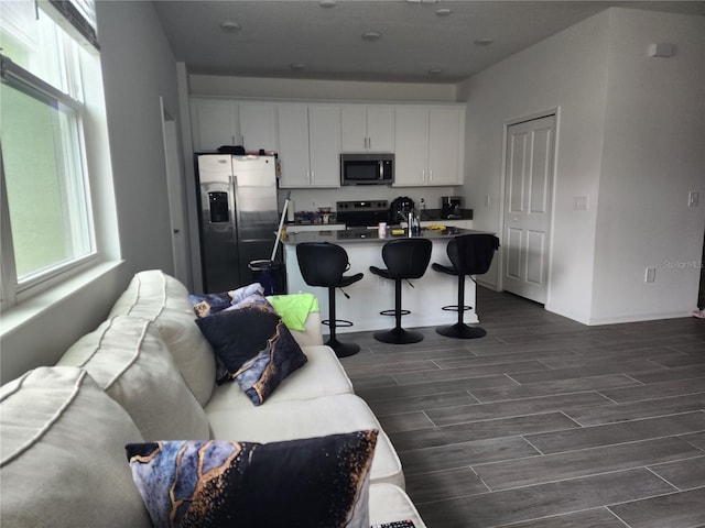 kitchen with stainless steel appliances, a kitchen breakfast bar, an island with sink, white cabinets, and dark wood-type flooring