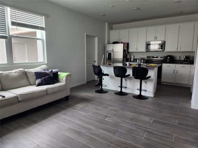 kitchen featuring stainless steel appliances, white cabinetry, a kitchen breakfast bar, a kitchen island with sink, and dark wood-type flooring