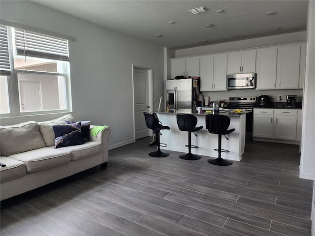 kitchen with a kitchen bar, dark hardwood / wood-style flooring, a center island with sink, white cabinets, and appliances with stainless steel finishes