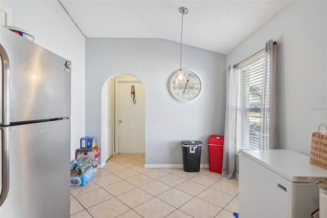 kitchen with stainless steel fridge, fridge, light tile patterned floors, hanging light fixtures, and lofted ceiling