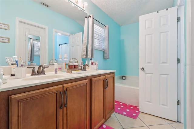 bathroom featuring tile patterned flooring, vanity, a textured ceiling, and tiled tub