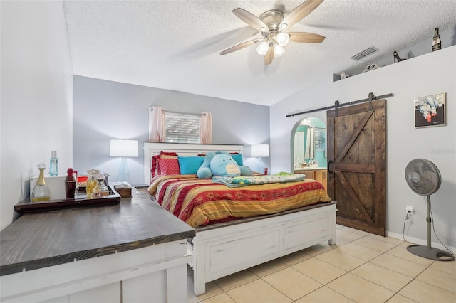 bedroom with a barn door, ceiling fan, light tile patterned floors, and a textured ceiling