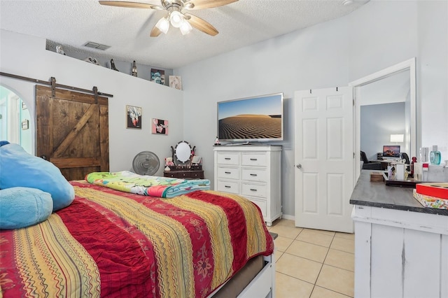 tiled bedroom with a barn door, ceiling fan, and a textured ceiling