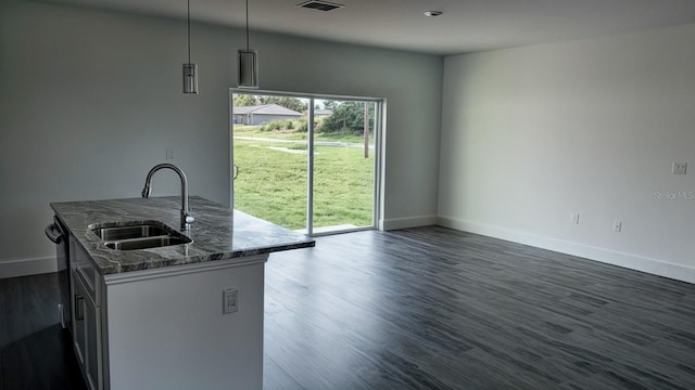 kitchen featuring a center island with sink, hanging light fixtures, dark stone countertops, dark hardwood / wood-style floors, and sink