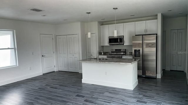 kitchen with light stone countertops, appliances with stainless steel finishes, white cabinetry, dark wood-type flooring, and a kitchen island with sink