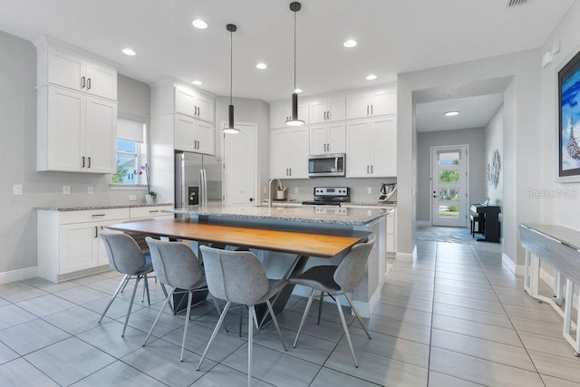 kitchen with appliances with stainless steel finishes, white cabinets, light stone counters, and a center island with sink