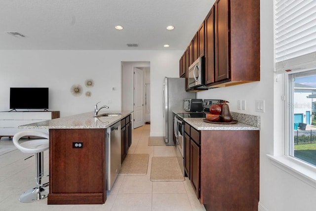 kitchen with light stone countertops, a kitchen island with sink, a kitchen bar, sink, and stainless steel appliances