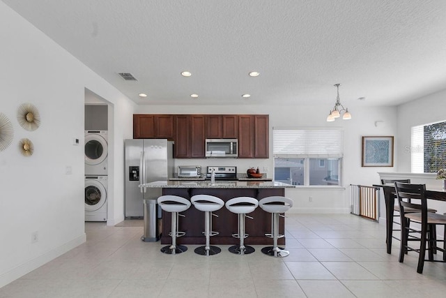 kitchen featuring a center island with sink, a kitchen bar, stacked washer and dryer, a notable chandelier, and stainless steel appliances