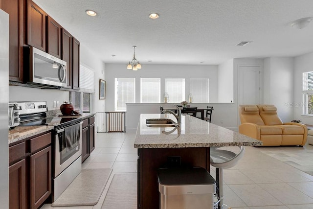 kitchen featuring appliances with stainless steel finishes, an inviting chandelier, a kitchen island with sink, pendant lighting, and sink