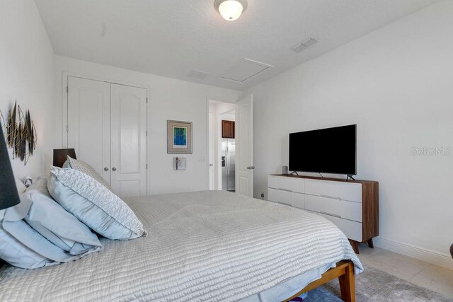 bedroom with stainless steel fridge with ice dispenser, a closet, and light tile patterned floors