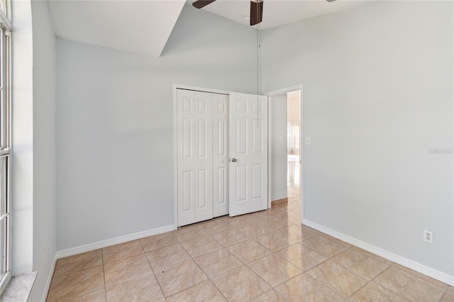 unfurnished bedroom with a towering ceiling, a closet, light tile patterned floors, and ceiling fan