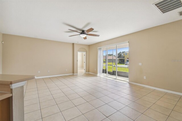 spare room featuring arched walkways, light tile patterned flooring, baseboards, visible vents, and a ceiling fan