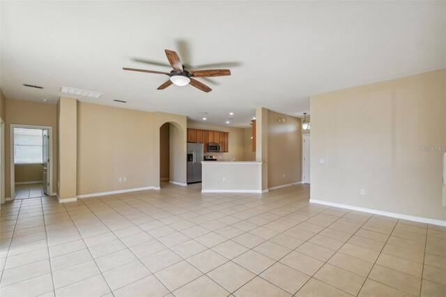 unfurnished living room with a ceiling fan, visible vents, arched walkways, and light tile patterned flooring