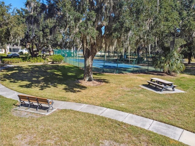 view of property's community with a lawn, fence, and a tennis court