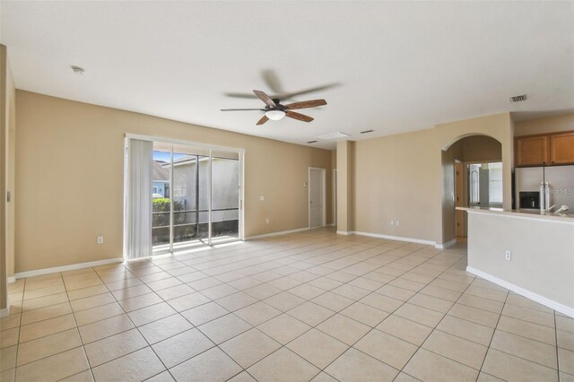 unfurnished living room featuring arched walkways, light tile patterned flooring, baseboards, visible vents, and a ceiling fan
