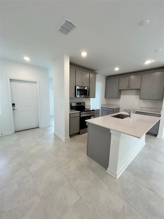 kitchen with gray cabinets, sink, appliances with stainless steel finishes, and a kitchen island with sink