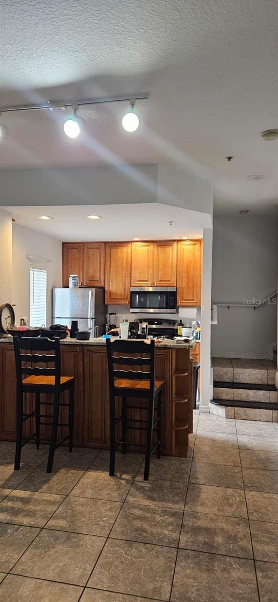 kitchen featuring dark tile patterned flooring, appliances with stainless steel finishes, a textured ceiling, and a kitchen breakfast bar