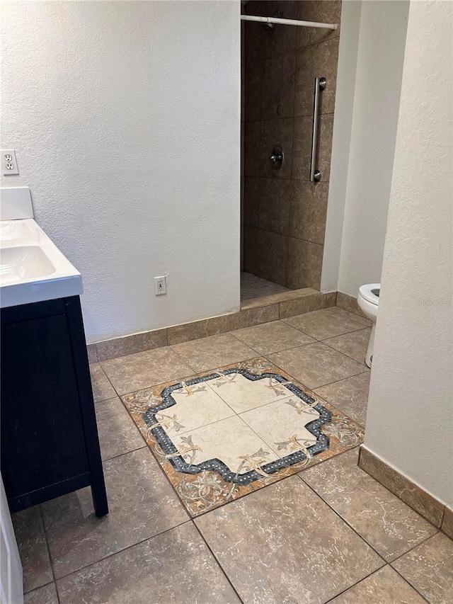 bathroom with toilet, vanity, tile patterned floors, and tiled shower