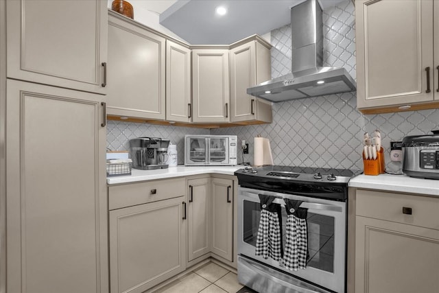 kitchen with cream cabinets, wall chimney exhaust hood, backsplash, light tile patterned flooring, and stainless steel range with electric cooktop