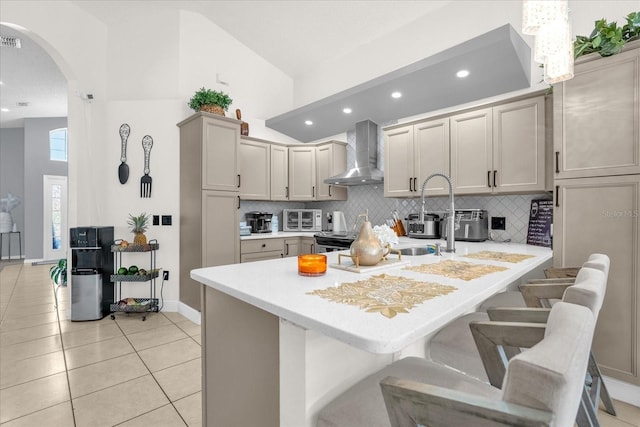 kitchen featuring gray cabinetry, light tile patterned floors, wall chimney exhaust hood, vaulted ceiling, and a breakfast bar area