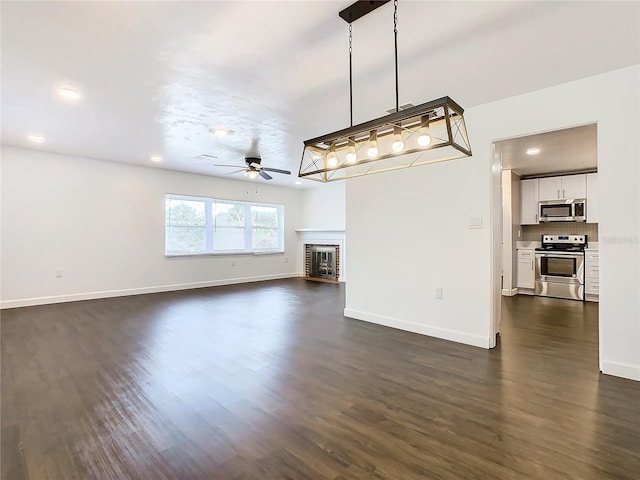 unfurnished living room with ceiling fan, a brick fireplace, and dark hardwood / wood-style flooring