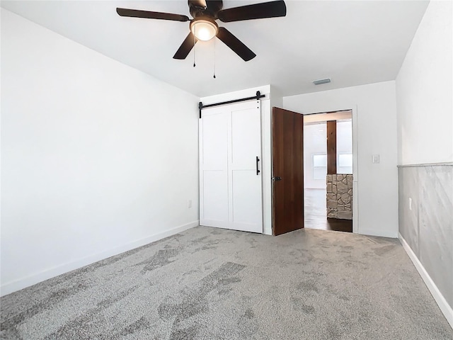 unfurnished bedroom featuring a barn door, carpet flooring, and ceiling fan