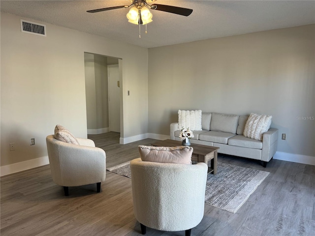 living area featuring visible vents, a textured ceiling, wood finished floors, baseboards, and ceiling fan