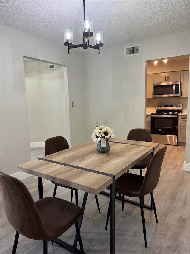 dining space featuring a chandelier, visible vents, light wood-style flooring, and a textured ceiling