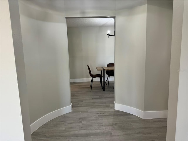 hall featuring wood finished floors, baseboards, and a textured ceiling