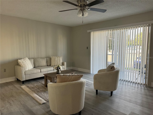 living room featuring a ceiling fan, wood finished floors, baseboards, and a textured ceiling