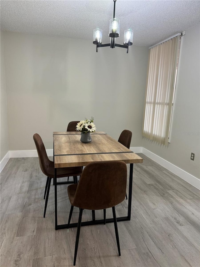 dining area with a chandelier, a textured ceiling, baseboards, and wood finished floors