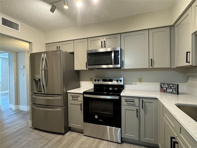 kitchen with a textured ceiling, appliances with stainless steel finishes, and gray cabinetry