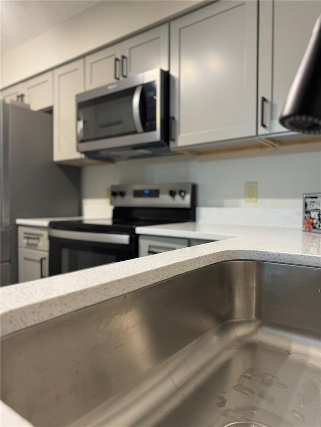 kitchen featuring a sink, light stone countertops, appliances with stainless steel finishes, and gray cabinetry